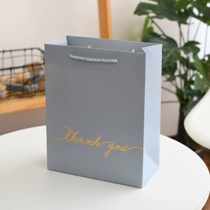 Close-up of a light blue starry gift bag with golden Thank You text and woven handles