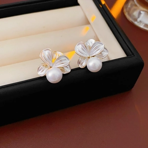 Détail de boucles d'oreilles fleur et perle avec bords dorés dans un écrin à bijoux noir