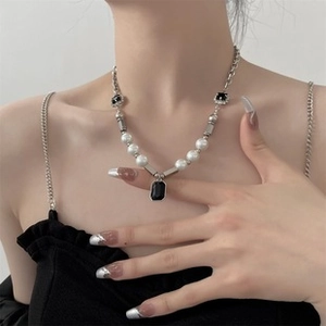 Detail of silver chain necklace with white pearls and black rectangular gemstones