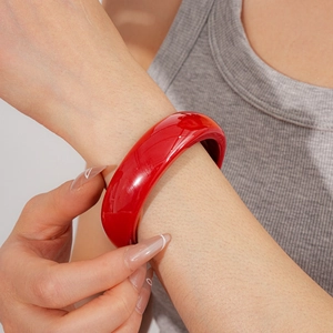 Bracelet jonc large en résine rouge brillant porté au poignet avec une finition polie chic