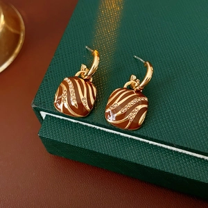 Detailed macro of gold striped earrings with brown enamel and sparkling crystals