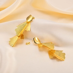 Macro shot of golden fan leaf tassel earrings displayed on champagne wrinkled silk fabric