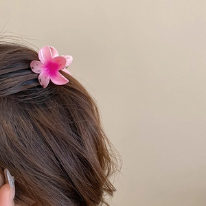 Detail showing a gradient pink flower hair claw clip styled on wavy brown hair