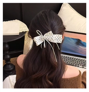Détail d'une pince à cheveux nœud en ruban à pois blancs sur de longs cheveux bruns ondulés