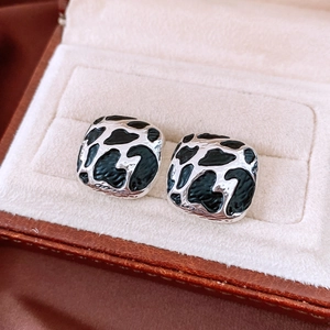 Macro shot of square silver earrings with black enamel pattern in a jewelry box