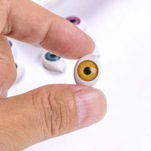 Macro view of a 12x16mm yellow acrylic doll eye held between fingers for scale