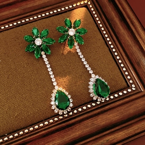 Detailed close-up of golden floral earrings with green teardrop stones on brown velvet