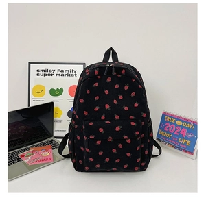 Detailed view of black corduroy backpack with strawberry patterns on a study desk