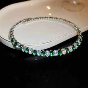 Detail of silver necklace with oval green and white zircons on a white ceramic plate