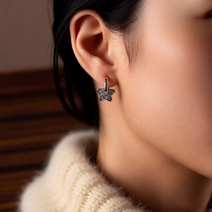 Close-up of a silver star charm earring on a model wearing a cozy beige knit sweater