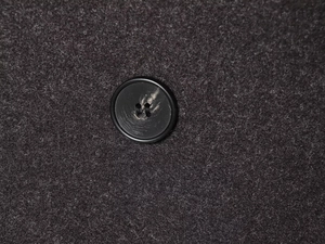 Close-up detail of a classic black round button on textured wool blend fabric coat