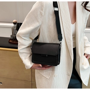 Close-up of black crossbody square bag with wide nylon strap on model in beige blazer