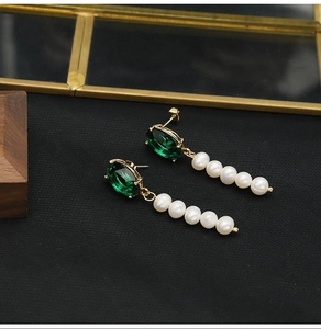 Detail of drop earrings with dark green stones and five dangling white pearls in gold