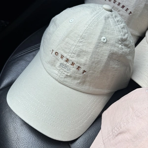 Dettaglio del cappellino beige chiaro con ricamo JOURNEY 007 e occhielli in metallo
