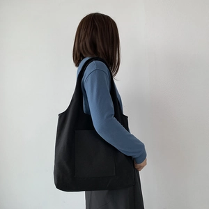 Detail of black canvas tote bag with a large front pocket worn by a female model