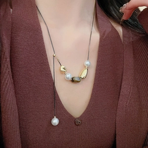Détail du pendentif en œil de tigre et collier de perles sur un cardigan marron