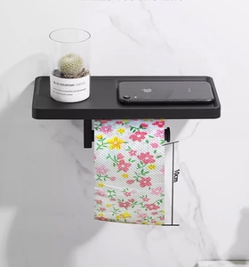 Wall-mounted matte black toilet paper holder with floral roll and top phone storage shelf