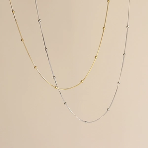 Close-up of gold and silver snake bone necklaces with beads on beige background