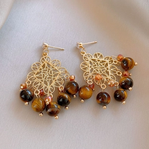 Detailed macro view of vintage gold hollow earrings with brown tiger eye stones and beads