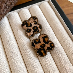 Detailed close-up of clover-shaped leopard print earrings on a beige velvet jewelry box