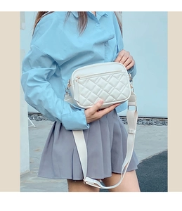 Detail of white quilted crossbody bag with gold zippers and wide fabric shoulder strap