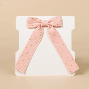 Detail of pink corduroy hair bow with gold polka dots on a white display card