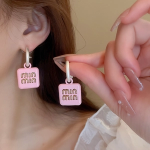 Close-up of pink square stud earrings with embossed lettering on a model's ear