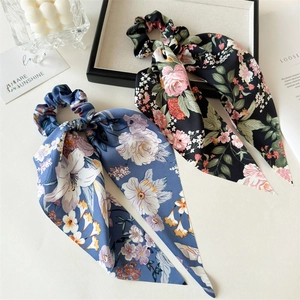 Detailed view of two elegant floral satin hair scrunchies with long ribbons on white tray