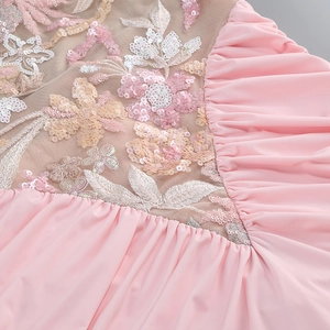 Dettaglio di paillettes champagne e ricami floreali bianchi su rete rosa del vestito