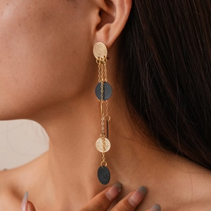 Close-up of gold chain earrings with textured black discs on a model for high-end fashion