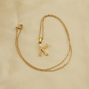 Gold stainless steel necklace with bamboo texture letter K pendant on satin fabric