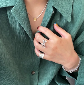Close-up of a silver bow ring and wave texture ring with a gold H pendant necklace