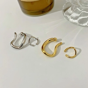 Detailed view of silver and gold wave-shaped ear cuffs on a minimalist white surface