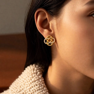 Detailed close-up of woven gold stud earrings with zircons on an elegant female model