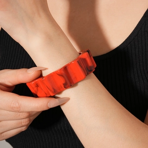 Detail of chunky orange-red marble resin bangle with wavy gear pattern on a wrist