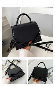 Detail of black faux leather handbag with chunky chain decor and adjustable shoulder strap