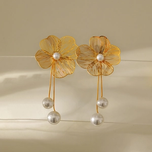 Detail of gold hollow flower earrings with hanging pearl pendants on transparent stand