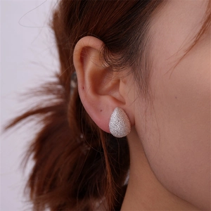 Detail view of silver teardrop stud earrings with textured caviar frosted finish on model