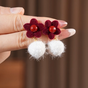 Detail of red flocked flower earrings with white plush pompom charms and soft velvet texture