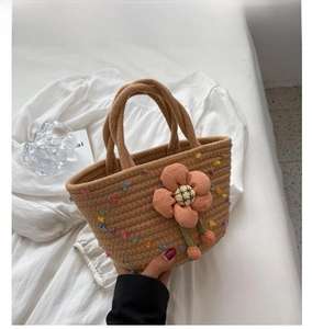 Detail of khaki woven handbag featuring a pink plush flower and colorful fiber accents