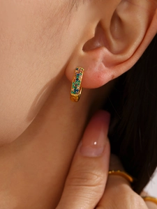Macro shot of gold hoop earrings with turquoise and zircon inlays worn on ear