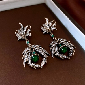 Detail of vintage bronze leaf earrings featuring green gems and crystals in royal style