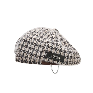 Houndstooth beret with a leather patch and silver chain detail on white background