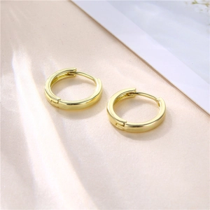Minimalist 18k gold plated round huggie hoop earrings displayed on soft silk background