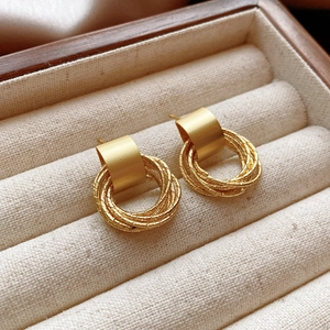 Close-up of vintage matte gold earrings with textured rings on a beige linen display