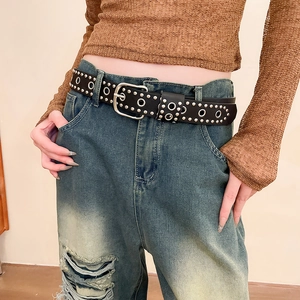 Détail d'une ceinture punk en cuir noir avec rivets et boucle métal sur un jean bleu