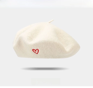 Detailed close-up of soft beige wool beret featuring delicate red heart embroidery