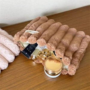 Brown plush makeup bag with pleated stripes and zipper closure on a wooden table