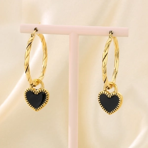 Close-up of golden twisted hoop earrings with black heart charms and serrated edges
