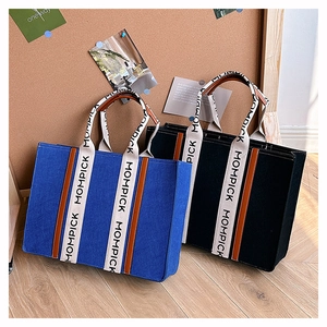 Detail view of large felt tote bags in blue and black with brown leather straps and Mompick text